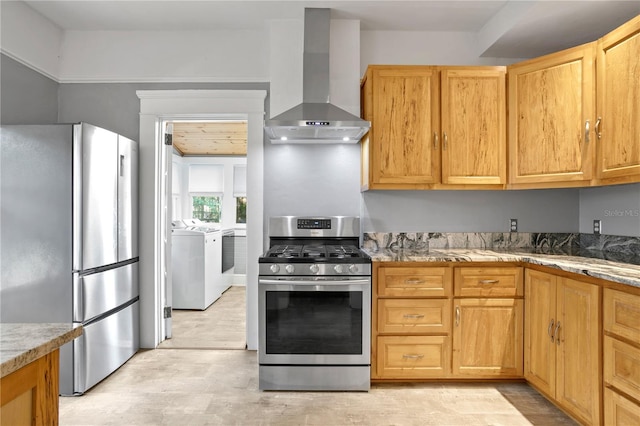 kitchen featuring washing machine and clothes dryer, light stone counters, wall chimney exhaust hood, and stainless steel appliances