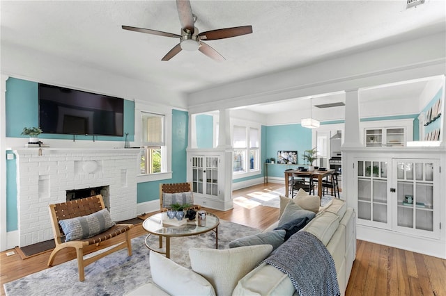 living room with ceiling fan, wood-type flooring, a textured ceiling, and a brick fireplace