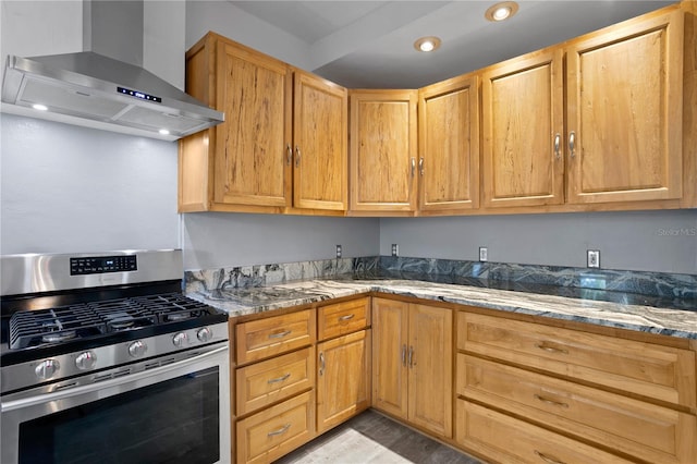 kitchen featuring wall chimney range hood, light hardwood / wood-style flooring, dark stone counters, and gas range