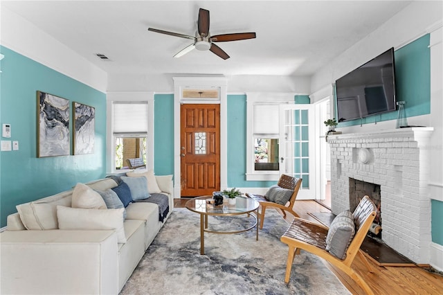 living room with ceiling fan, light wood-type flooring, and a brick fireplace