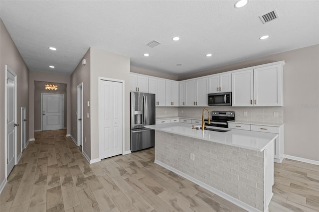 kitchen featuring light wood-type flooring, sink, white cabinetry, stainless steel appliances, and a center island with sink