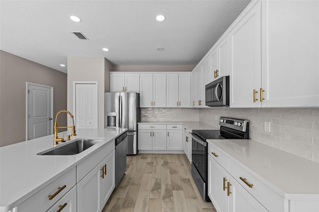 kitchen with a center island with sink, sink, stainless steel appliances, and white cabinets