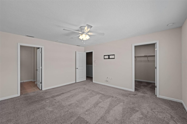 unfurnished bedroom featuring a spacious closet, a closet, a textured ceiling, ceiling fan, and light colored carpet