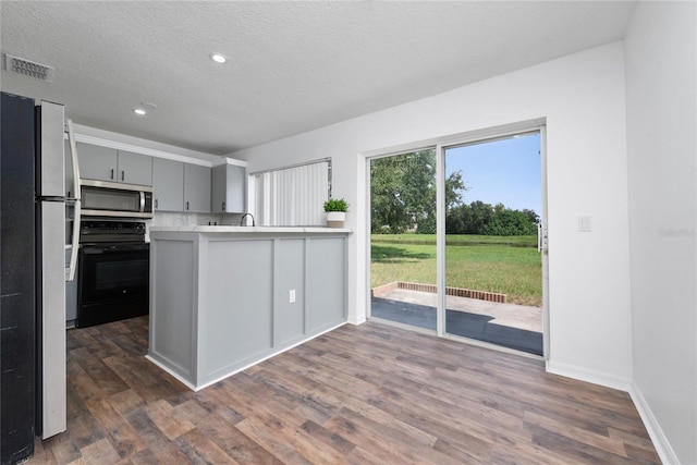 kitchen with gray cabinetry, black stove, dark wood-type flooring, kitchen peninsula, and white fridge