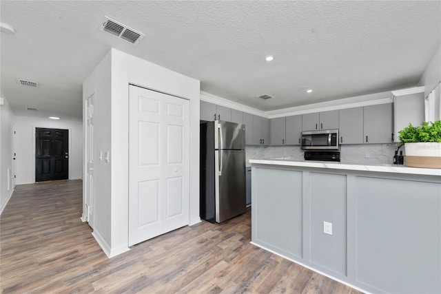 kitchen featuring wood-type flooring, kitchen peninsula, gray cabinetry, decorative backsplash, and appliances with stainless steel finishes