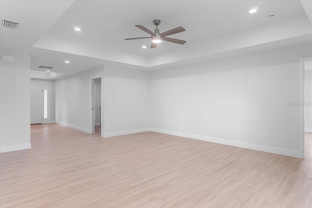 spare room with ceiling fan, light hardwood / wood-style flooring, and a raised ceiling