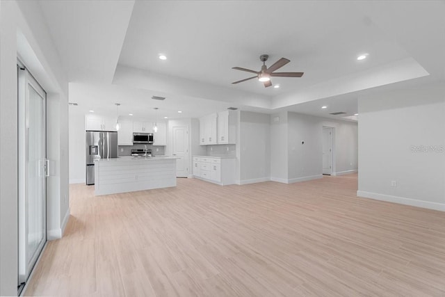 unfurnished living room with light wood-type flooring, ceiling fan, and a raised ceiling