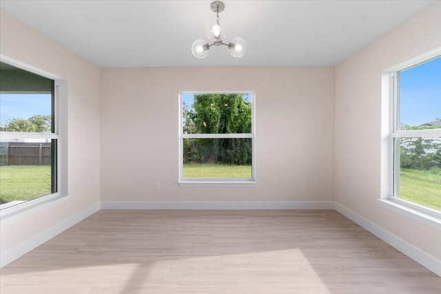 empty room featuring a notable chandelier and light wood-type flooring