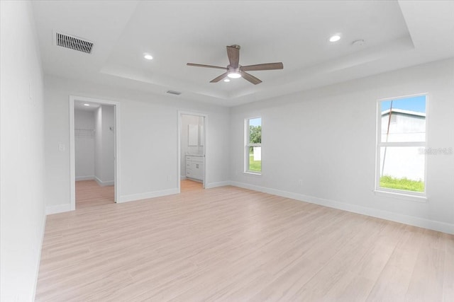 unfurnished bedroom featuring ceiling fan, a raised ceiling, light hardwood / wood-style floors, and a spacious closet