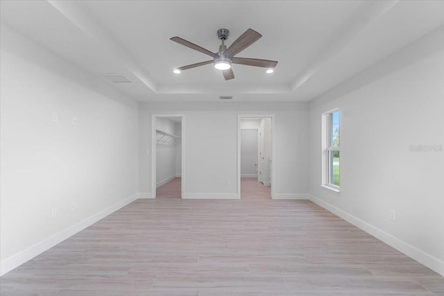 unfurnished bedroom featuring light hardwood / wood-style floors, a tray ceiling, ceiling fan, and a closet