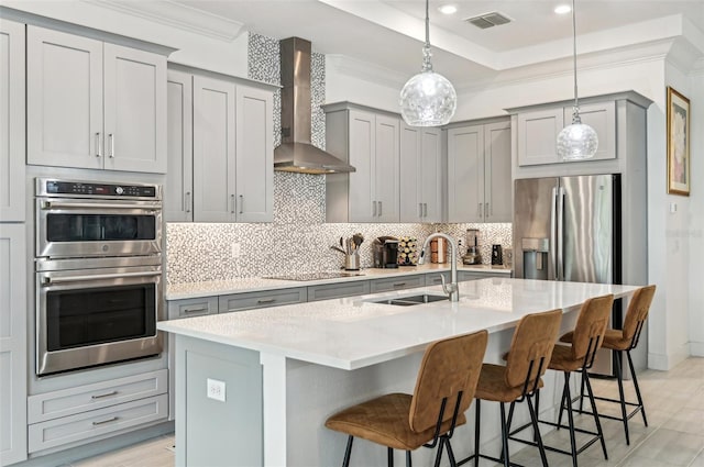 kitchen featuring pendant lighting, sink, a kitchen island with sink, wall chimney range hood, and appliances with stainless steel finishes