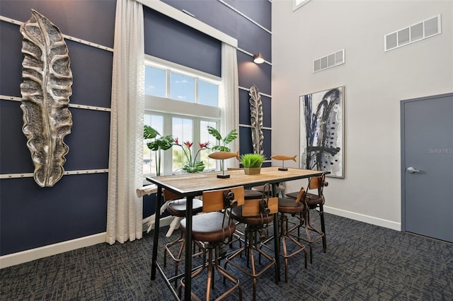 dining room featuring a towering ceiling and dark colored carpet