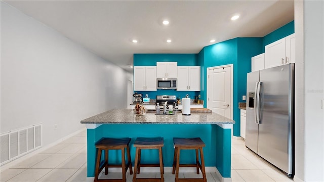 kitchen featuring stainless steel appliances, light tile patterned floors, visible vents, and a kitchen breakfast bar