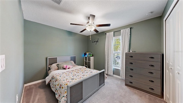 bedroom featuring ceiling fan, light colored carpet, a textured ceiling, and a closet