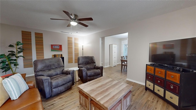 living room featuring light hardwood / wood-style flooring, ceiling fan, and a textured ceiling