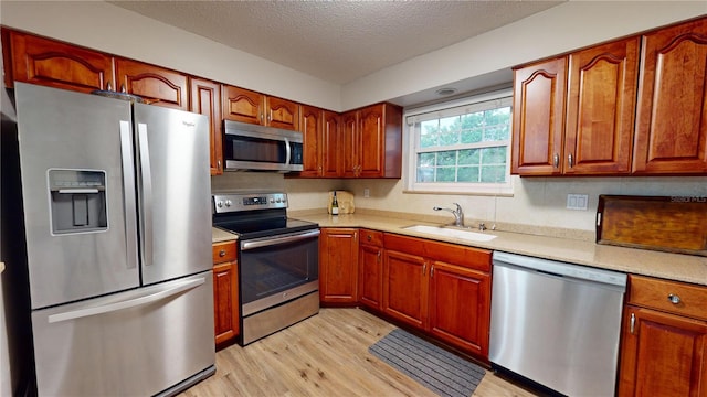 kitchen with a textured ceiling, appliances with stainless steel finishes, light wood-type flooring, and sink