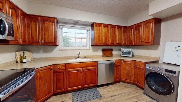 kitchen with stainless steel appliances, light wood-type flooring, sink, and washer / dryer