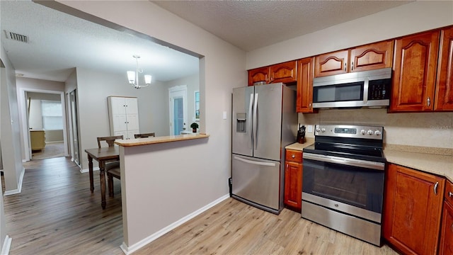 kitchen featuring hanging light fixtures, light hardwood / wood-style floors, stainless steel appliances, a textured ceiling, and a notable chandelier