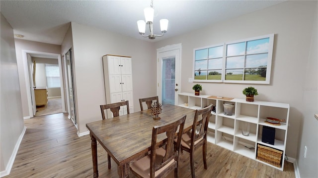 dining space featuring a textured ceiling, light wood-type flooring, a chandelier, and a healthy amount of sunlight