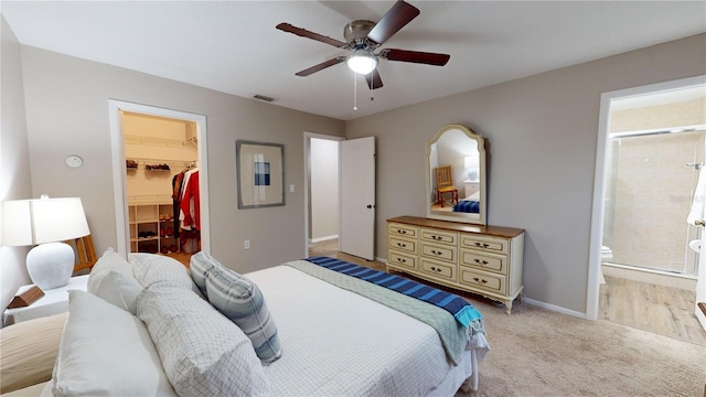 bedroom featuring connected bathroom, a closet, ceiling fan, a walk in closet, and light carpet