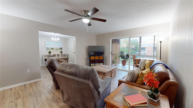 living room with light wood-type flooring, ceiling fan with notable chandelier, plenty of natural light, and a textured ceiling