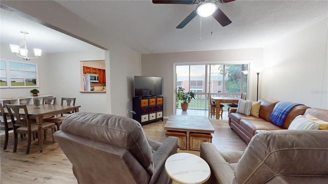 living room featuring ceiling fan with notable chandelier, light hardwood / wood-style floors, and a textured ceiling