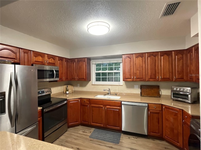 kitchen with washer / dryer, a textured ceiling, light hardwood / wood-style floors, sink, and appliances with stainless steel finishes