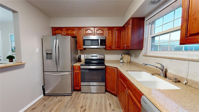 kitchen featuring a textured ceiling, appliances with stainless steel finishes, light wood-type flooring, and sink