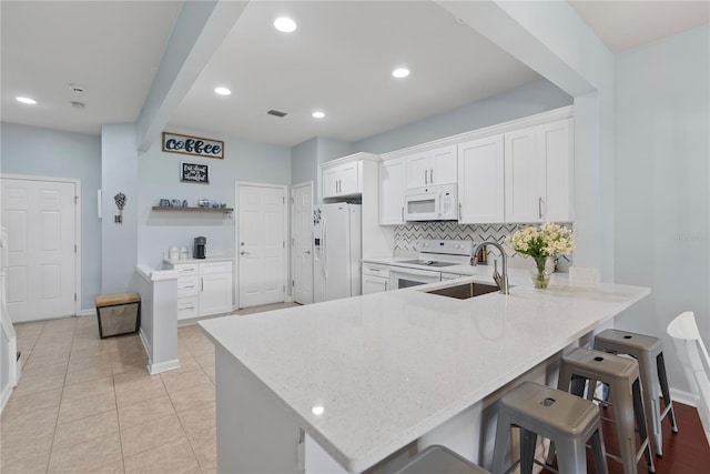 kitchen featuring white appliances, white cabinets, a kitchen breakfast bar, sink, and kitchen peninsula