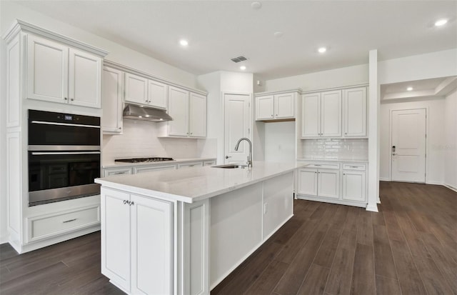 kitchen featuring white cabinets, double oven, a kitchen island with sink, and sink