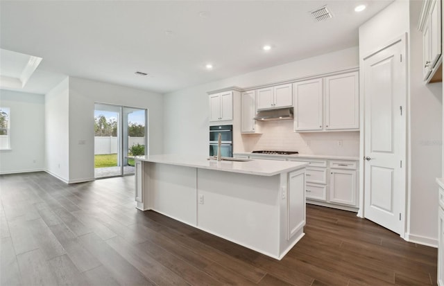 kitchen featuring backsplash, white cabinets, sink, an island with sink, and gas cooktop