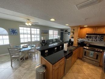 kitchen featuring a textured ceiling, kitchen peninsula, appliances with stainless steel finishes, light tile patterned floors, and ceiling fan