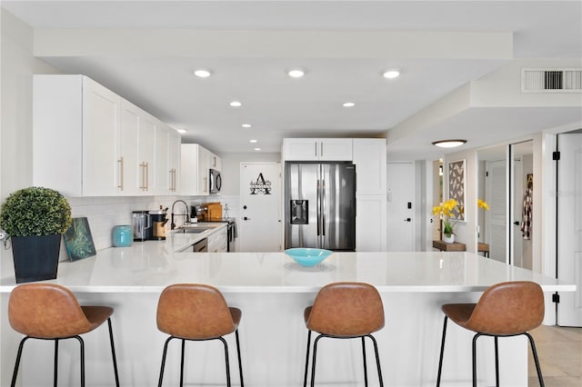 kitchen with tasteful backsplash, white cabinets, kitchen peninsula, appliances with stainless steel finishes, and a kitchen breakfast bar