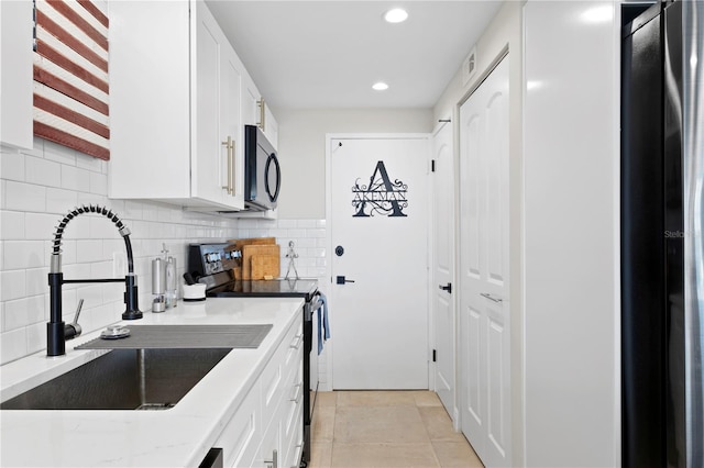 kitchen featuring light tile patterned flooring, sink, light stone counters, white cabinets, and appliances with stainless steel finishes