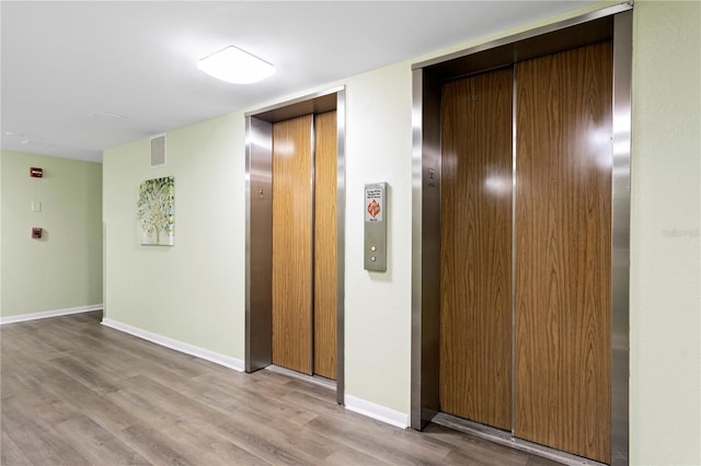 hallway with elevator and light hardwood / wood-style flooring