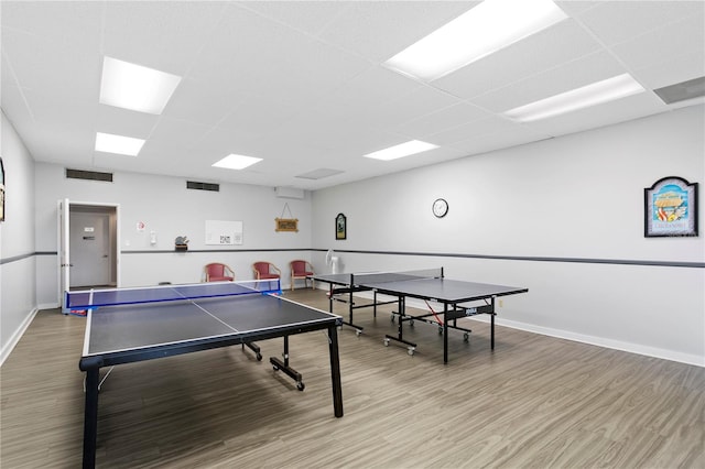 recreation room with hardwood / wood-style flooring, a paneled ceiling, and an AC wall unit