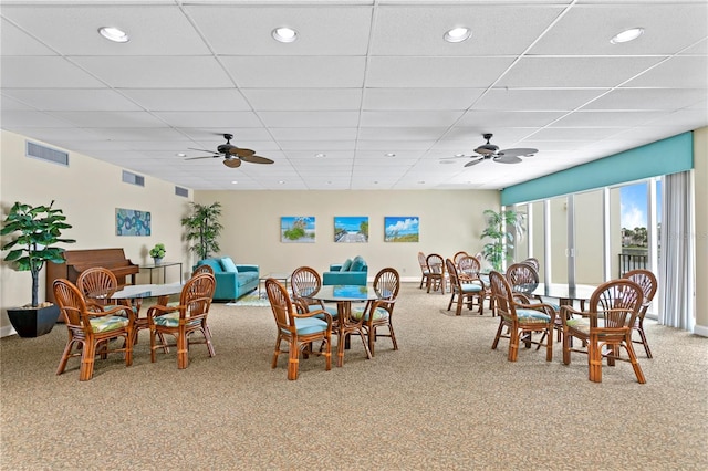 dining area with a drop ceiling, light carpet, and ceiling fan