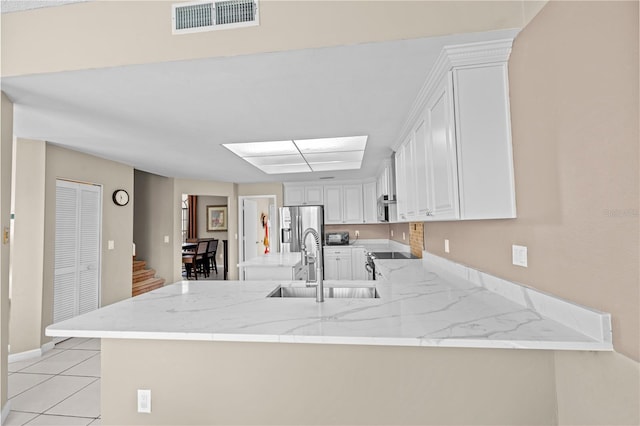 kitchen with light stone counters, sink, kitchen peninsula, stainless steel fridge with ice dispenser, and white cabinetry