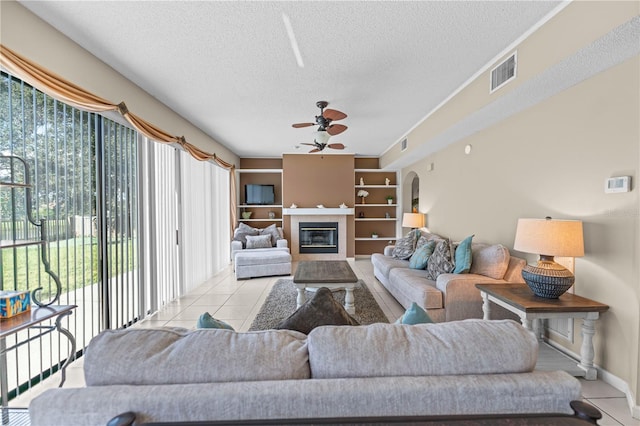 living room with a textured ceiling, light tile patterned floors, a tiled fireplace, and ceiling fan