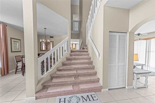 staircase with ceiling fan with notable chandelier, tile patterned flooring, and a textured ceiling