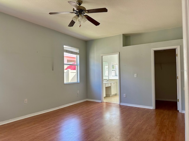 unfurnished bedroom with ensuite bathroom, ceiling fan, a spacious closet, hardwood / wood-style floors, and a closet