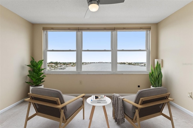 sitting room with light carpet, a textured ceiling, a water view, and plenty of natural light