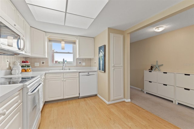 kitchen with backsplash, white cabinetry, a sink, white appliances, and light wood-style flooring