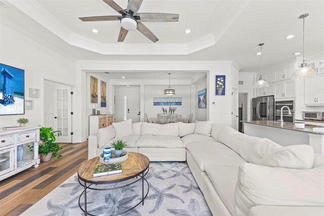 living room featuring ceiling fan, a raised ceiling, crown molding, and dark wood-type flooring