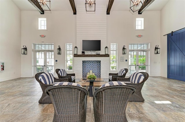 living room with a large fireplace, a chandelier, beamed ceiling, and a barn door