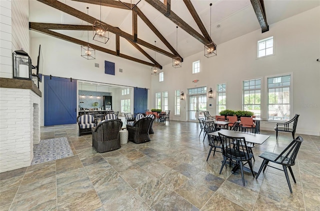 dining area featuring beamed ceiling, a barn door, high vaulted ceiling, and a wealth of natural light