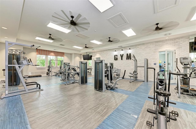 gym featuring light hardwood / wood-style floors, ceiling fan, and brick wall