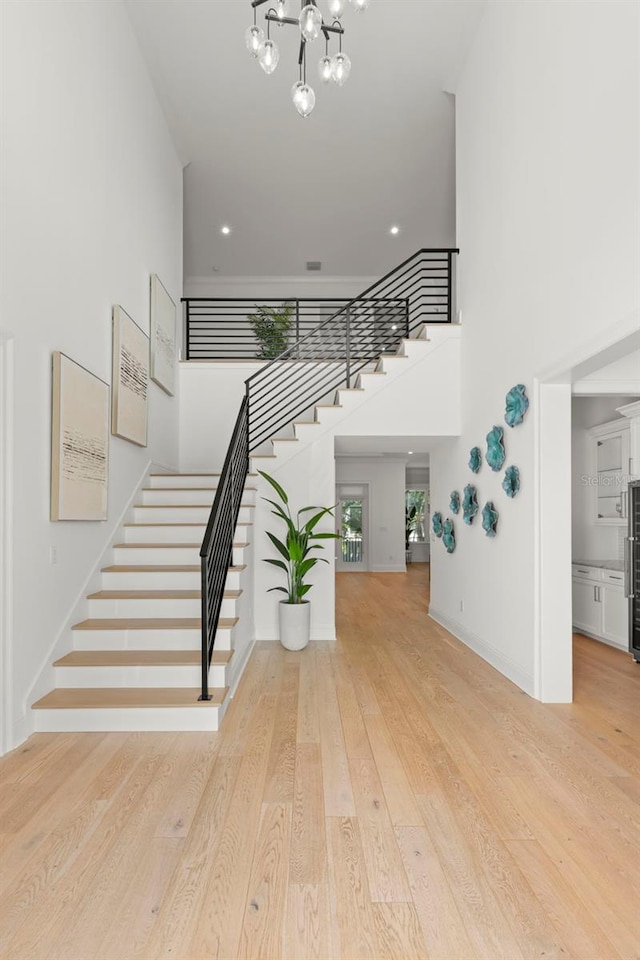 staircase with an inviting chandelier, wood-type flooring, and a high ceiling