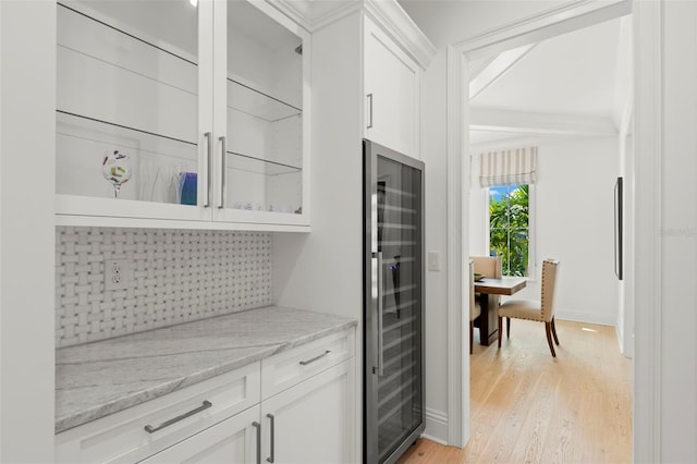 kitchen with light wood-type flooring, white cabinetry, wine cooler, and light stone counters