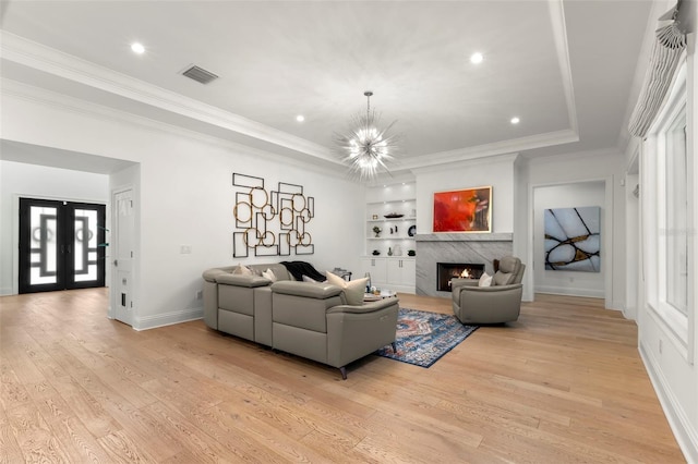 living room with light wood-type flooring, built in features, ornamental molding, and a chandelier